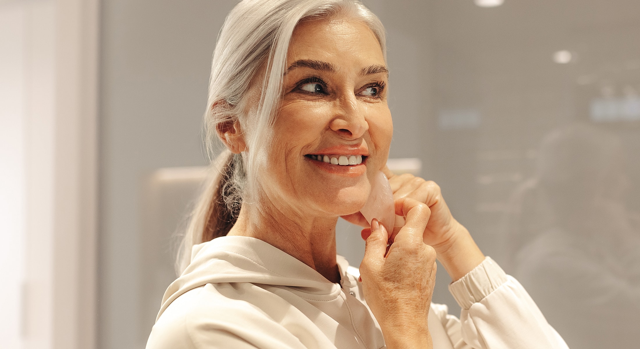 Woman using skincare tool while smiling at mirror.