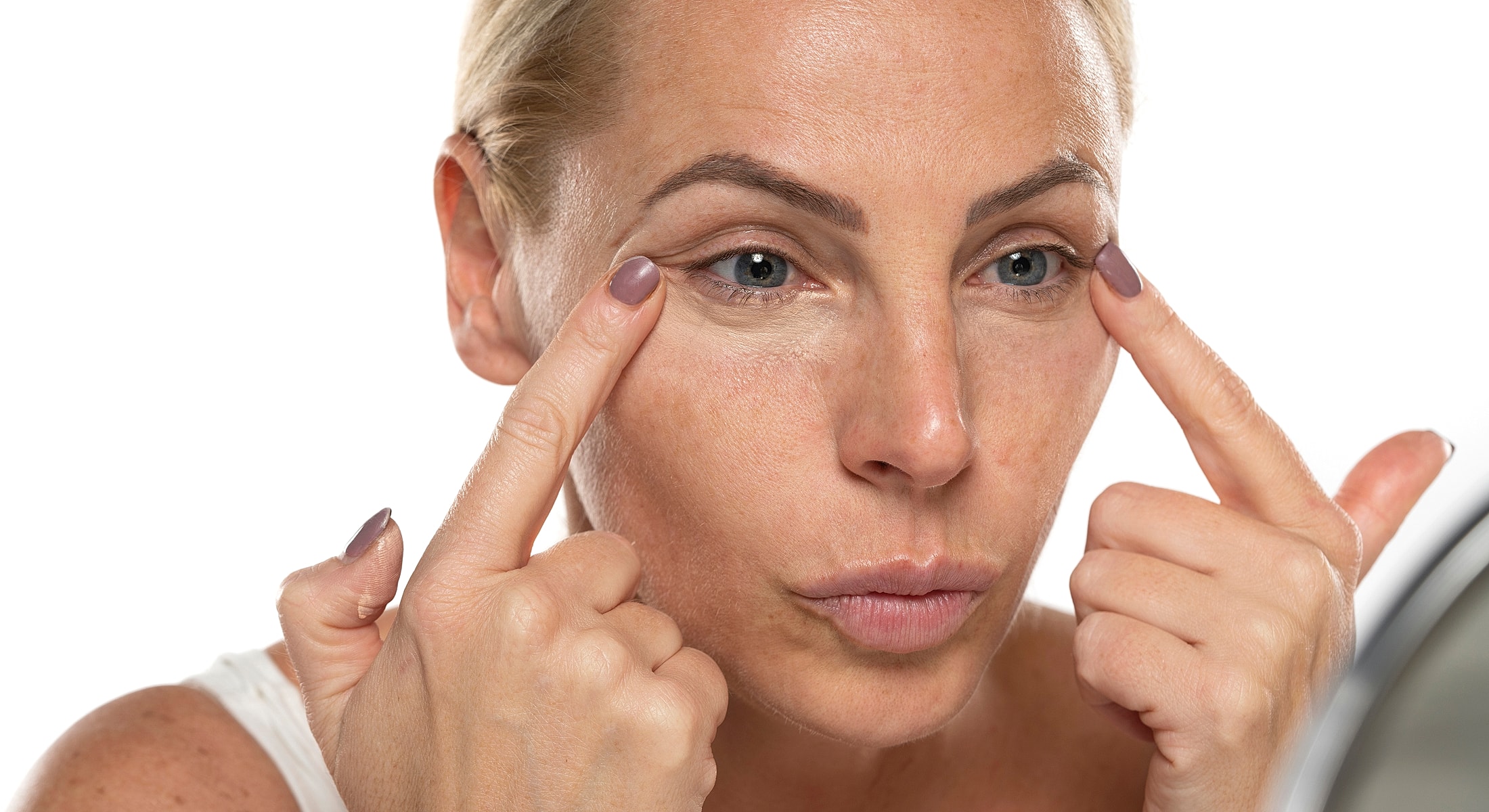 Woman applying skincare around her eyes.