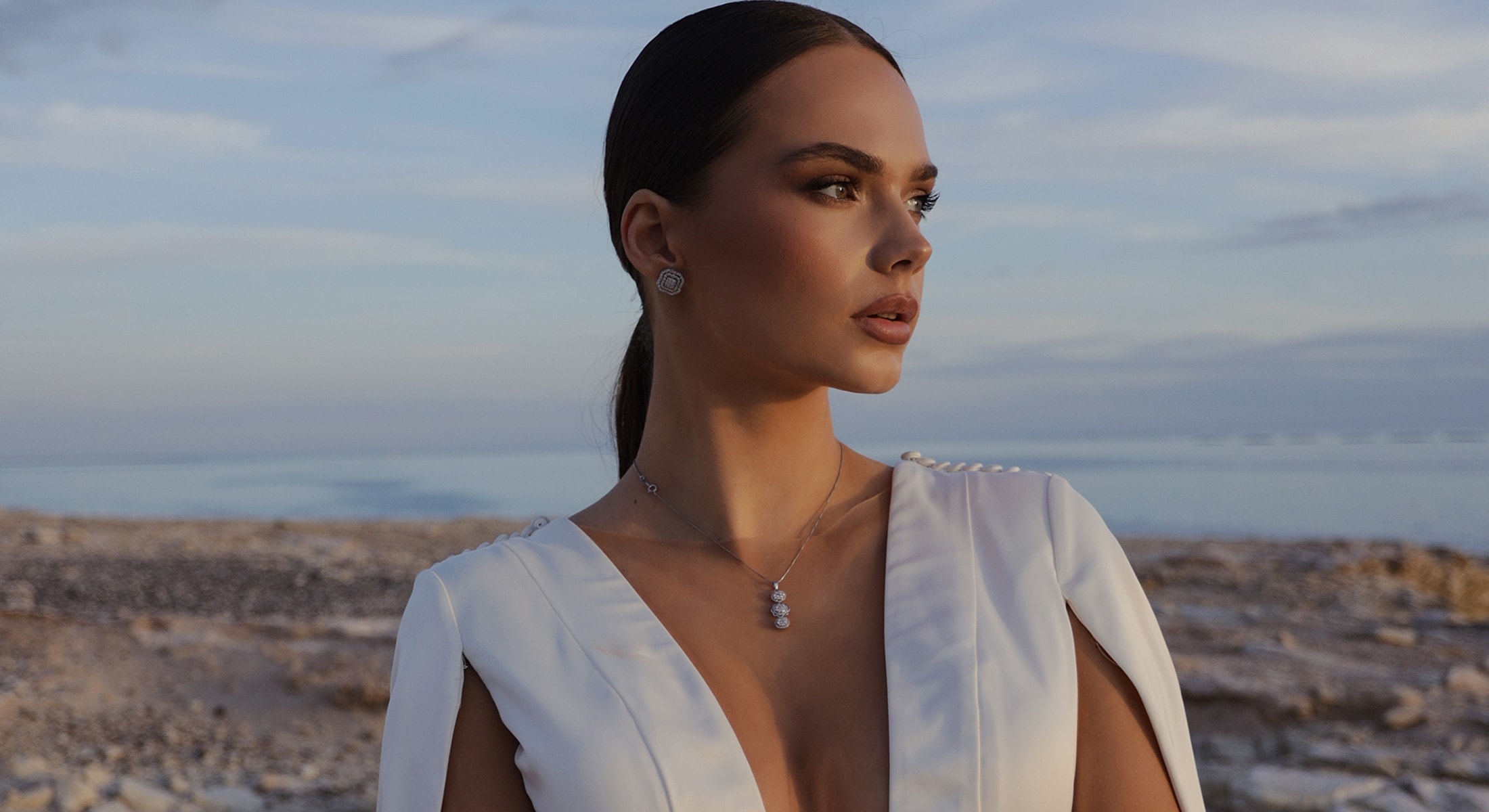 Model in elegant white dress by the seaside.