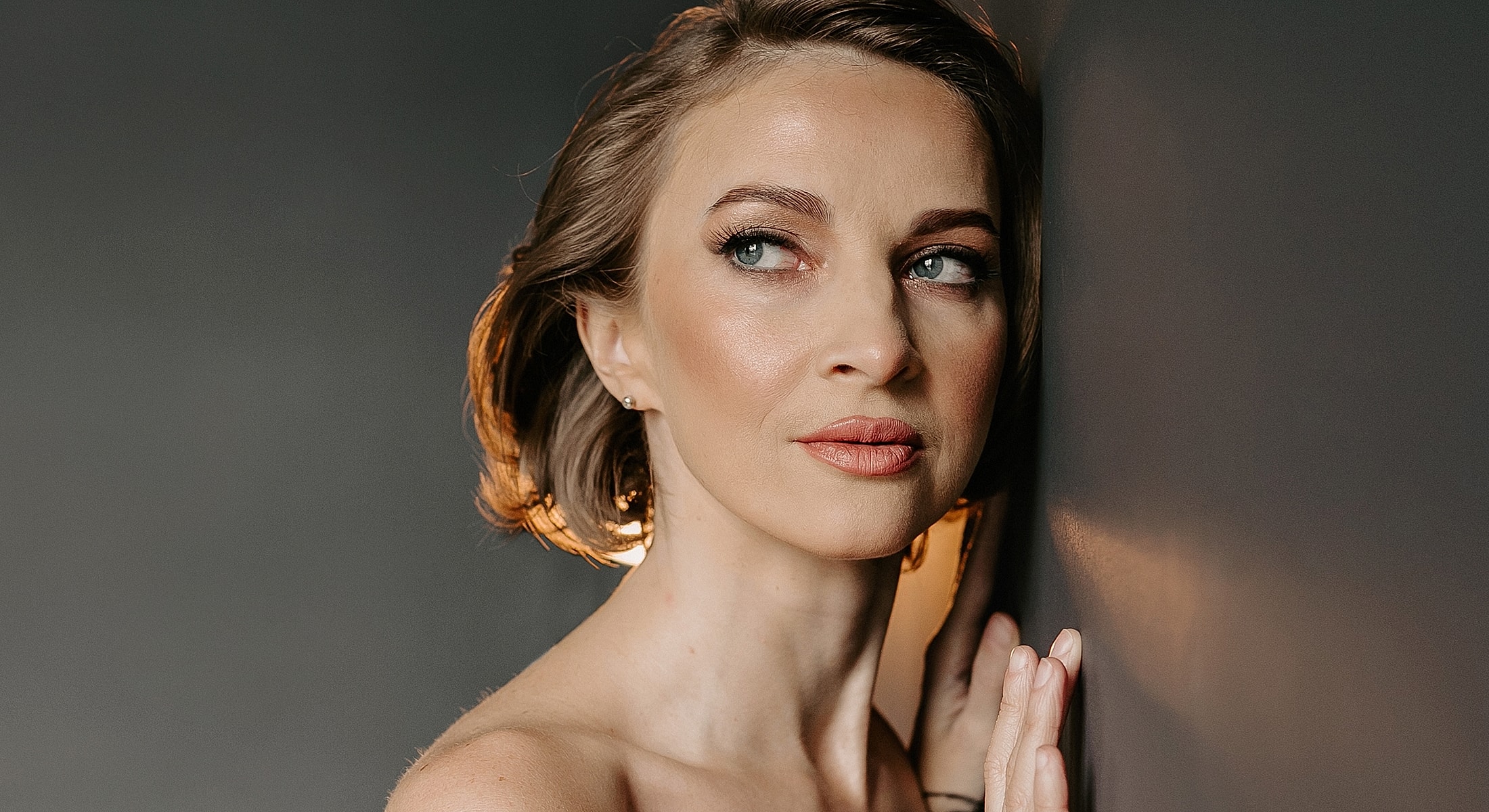Woman posing against a dark wall, thoughtful expression.