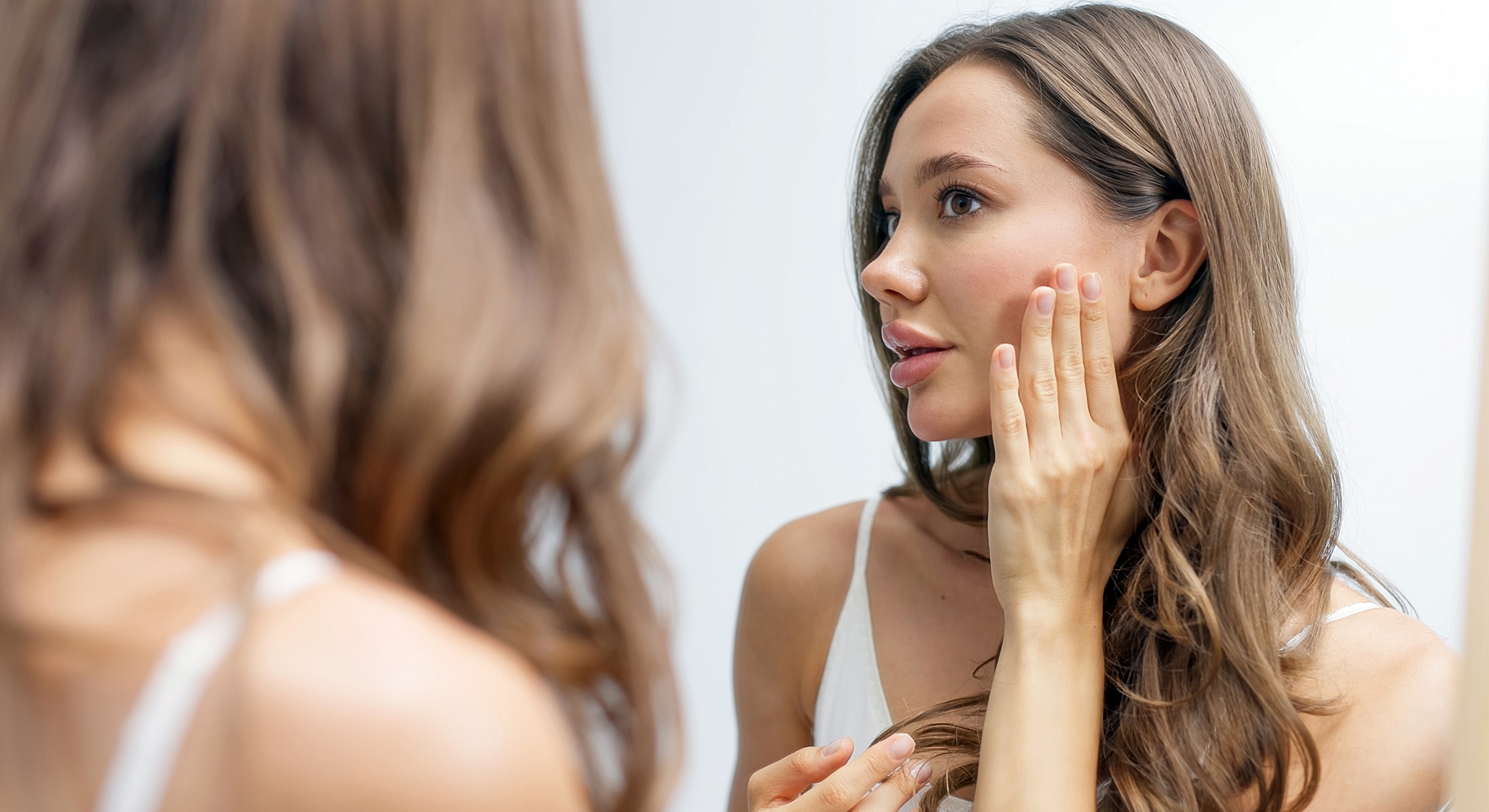 Woman examining her skin in a mirror.